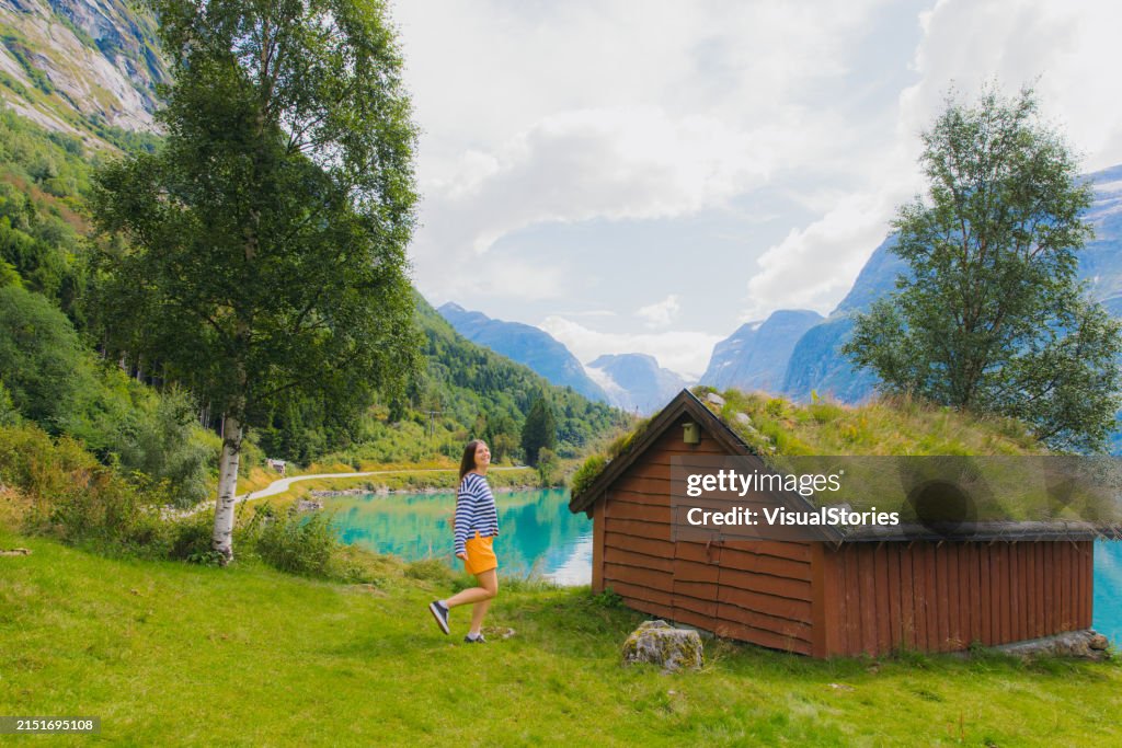 Happy Woman Tourist Walking in Mountain Village of Norway with Scenic Lake View