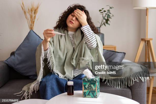 sick woman checking temperature on couch - meningitis stock pictures, royalty-free photos & images