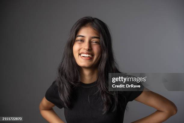 junges indisches mädchen lächelt vor grauem hintergrund - halbnahe-einstellung stock-fotos und bilder
