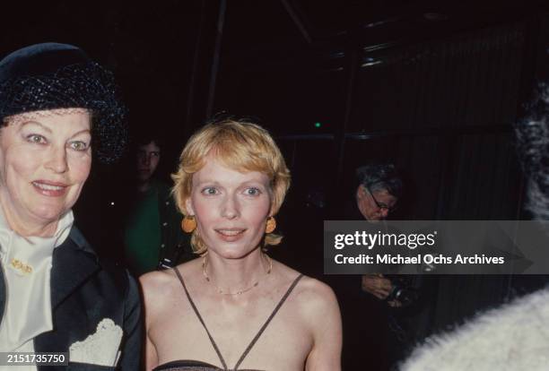 American actress Ava Gardner, wearing a black jacket over a white bow-front blouse and a black hat with a mesh veil, and American actress Mia Farrow,...