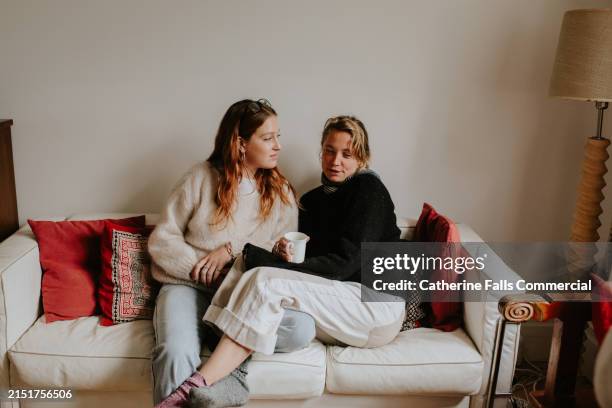two woman sit close together on a sofa having a serious discussion - gay couple stock pictures, royalty-free photos & images