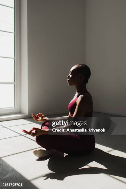 beautiful black woman in red sportswear practicing lotus asana in yoga studio. - meditation stock pictures, royalty-free photos & images