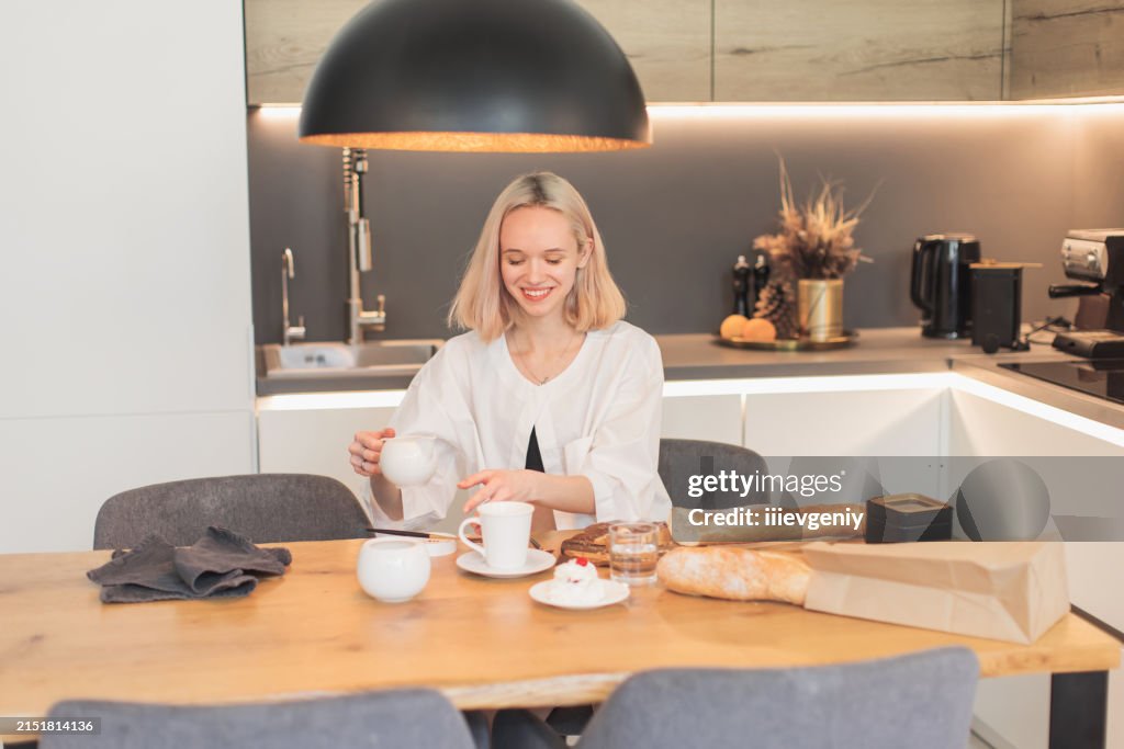 Young blonde woman pours cream into coffee.