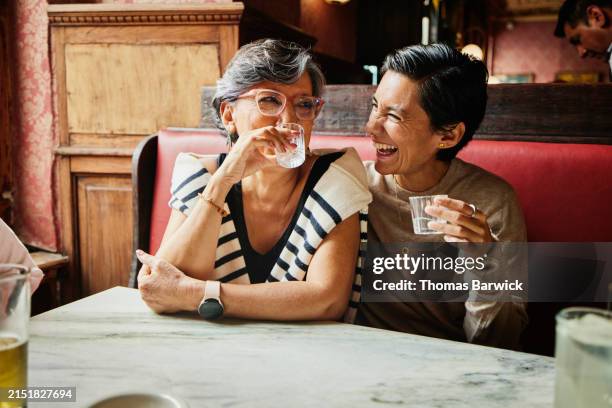 medium shot laughing daughter and mother sharing drinks in bar - halbnahe-einstellung stock-fotos und bilder