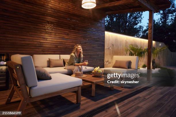 smiling woman enjoying in her drink during the evening on a patio. - patio stock pictures, royalty-free photos & images