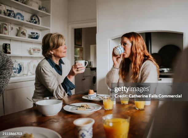 a mother and adult daughter drinking coffee in a stylish kitchen - refreshment table stock pictures, royalty-free photos & images
