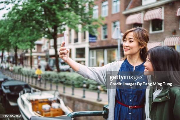 capturing memories: young asian mom taking selfie with her teenage daughter using smart phone while exploring in a new city - mit mobilgerät aufgenommen stock-fotos und bilder