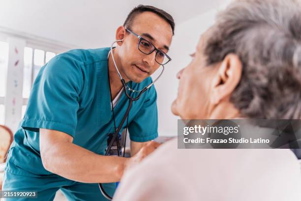 nurse listening heartbeat of a senior woman during medical consultation - krankenpfleger stock-fotos und bilder
