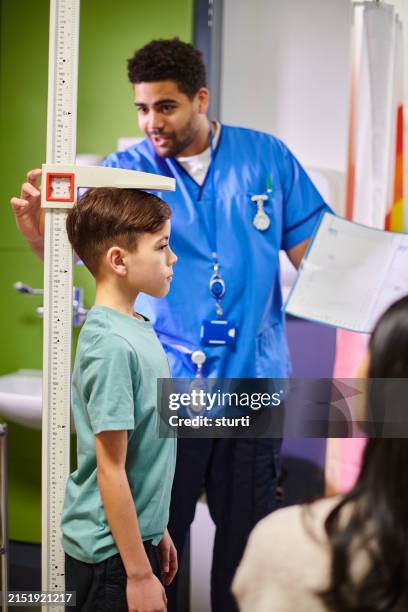 male nurse with mother and child patient looking at height chart - groeimeter stockfoto's en -beelden