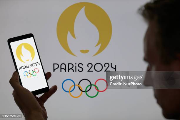 The Paris Olympic Games logo is being displayed on a smartphone with the Paris 2024 Olympic Games icon visible in the background in this photo...