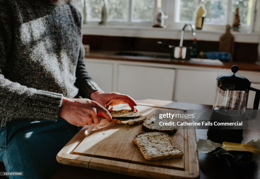 A man spreads butter onto lightly toasted bread in a domestic kitchen