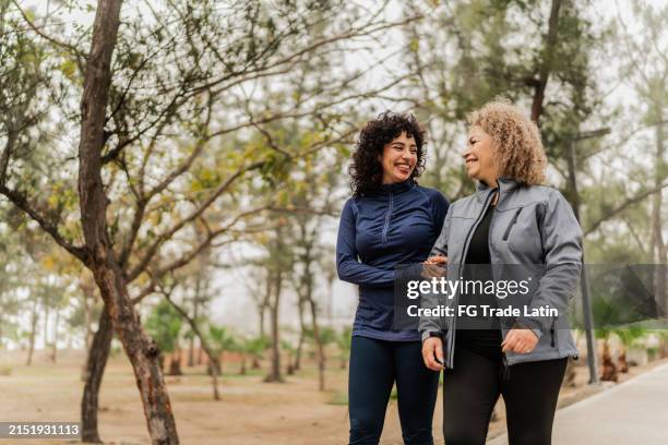 mother and daughter talking while walking through the public park - buitenopname stockfoto's en -beelden