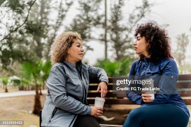 mother and daughter talking sitting on park bench at public park - banc public photos et images de collection