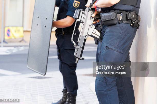 side view of two police officers standing in the street with riot guns and shields on a sunny day. - cuerpo de policía fotografías e imágenes de stock