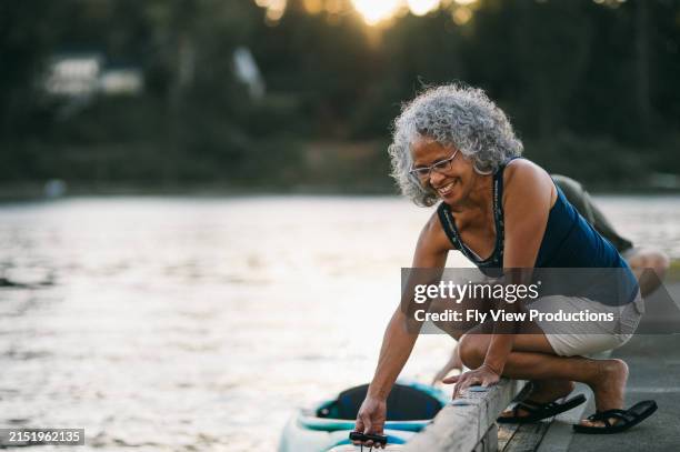 cheerful senior woman preparing to kayak on river at sunset - actieve ouderen stockfoto's en -beelden