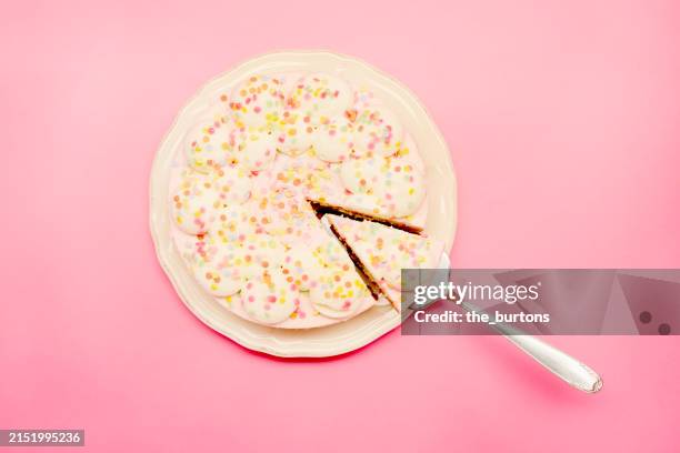 high angle view of a cream cake on a plate with cake server on pink background - taartpunt stockfoto's en -beelden