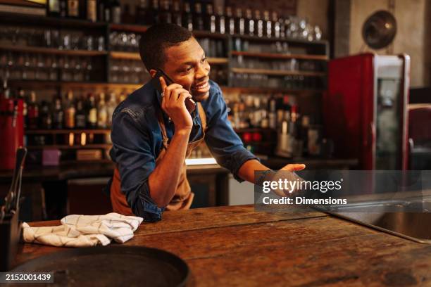 happy african-american barista is having a fun conversation over the phone. - the bartenders stock pictures, royalty-free photos & images