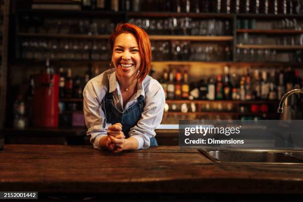 barmaid accoudée à un comptoir et riant dans un bar. - leaning on bar photos et images de collection