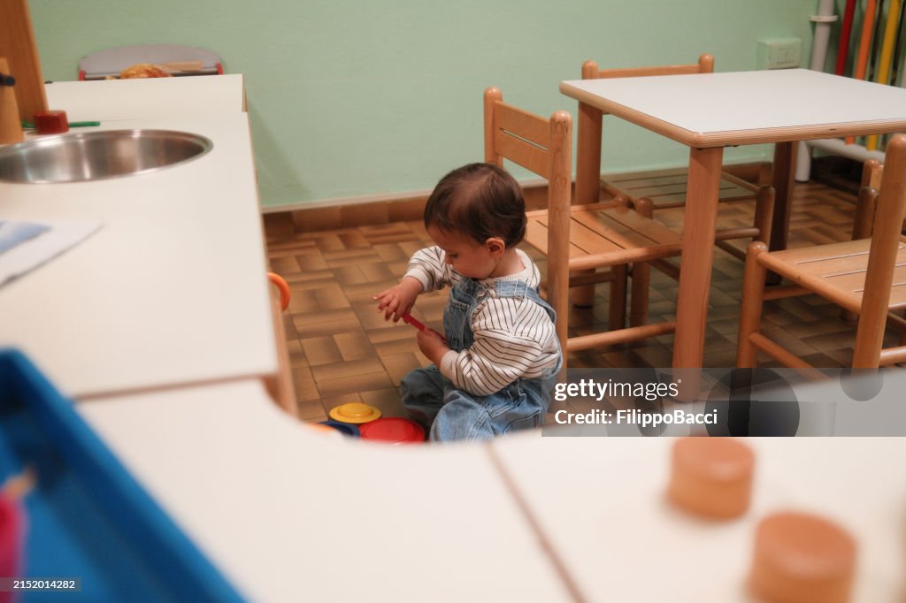 A baby boy is playing with a toy kitchen at the playroom