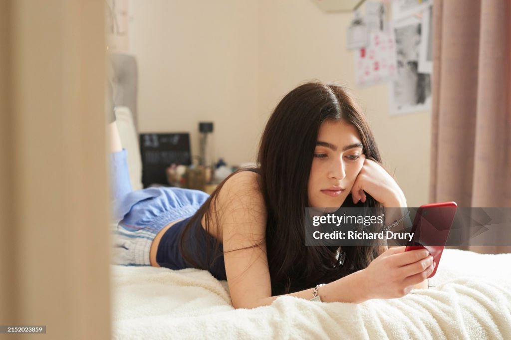Teenage girl lying on her bed and using a smart phone