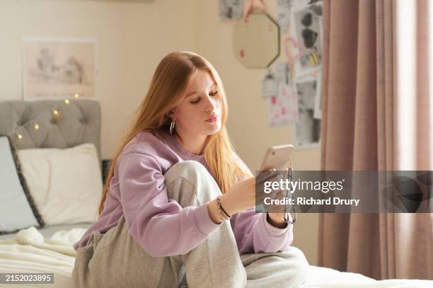teenage girl sitting cross legged on her bed and using a smartphone - chica adolescente fotografías e imágenes de stock