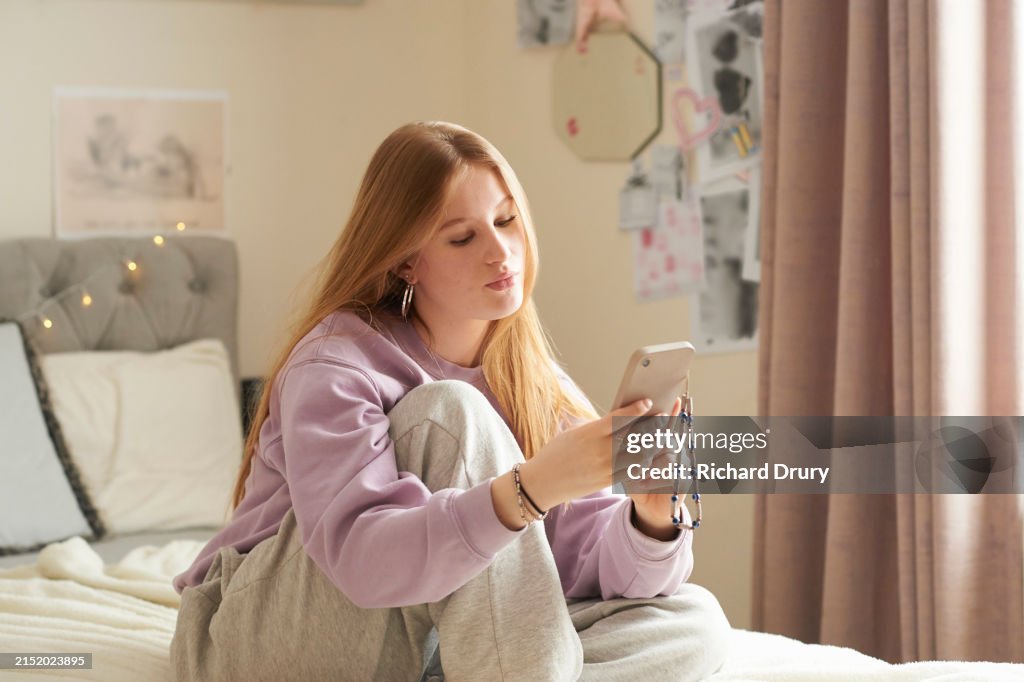 Teenage girl sitting cross legged on her bed and using a smartphone