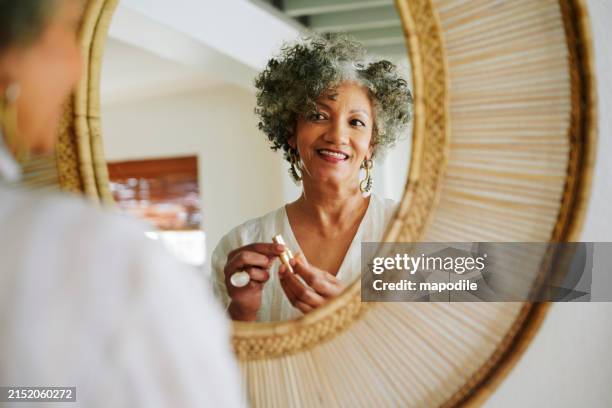 mulher madura sorridente colocando batom em um espelho em casa - um dia na vida - fotografias e filmes do acervo