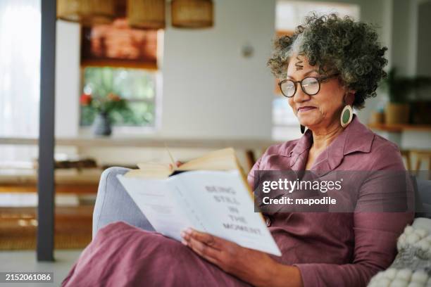 donna matura rilassante con un libro sul suo divano soggiorno - occhiali da lettura foto e immagini stock