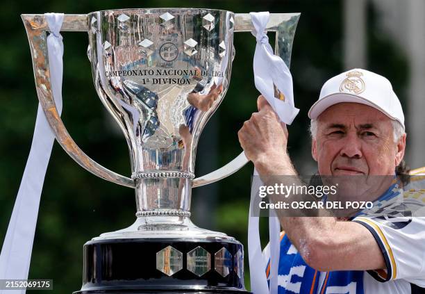 Real Madrid's Italian coach Carlo Ancelotti holds the 36th Spanish La Liga trophy of his team as Real Madrid players parade onboard a bus to...