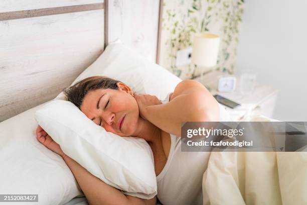 ritratto di una donna sdraiata a letto che si tocca il collo dolorante - malvagità foto e immagini stock
