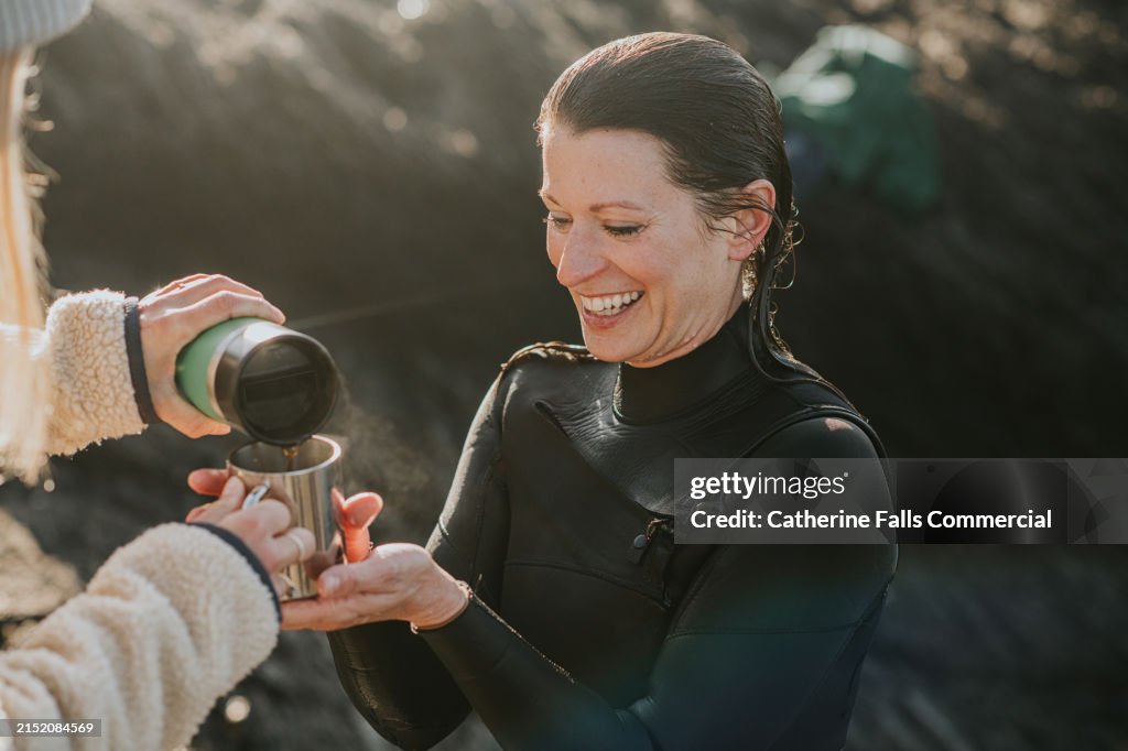 A woman is poured a hot drink from an insulated flask to warm up after cold water swimming