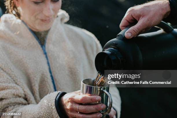 a woman is poured a hot drink from an insulated flask to warm up after cold water swimming - tea hot drink stock pictures, royalty-free photos & images