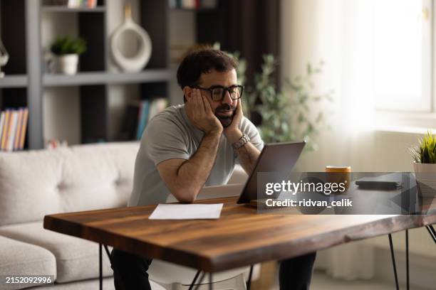 a stressed freelance man sighing and looking at his tablet for work while sitting backwards on a chair. - sighing stock pictures, royalty-free photos & images