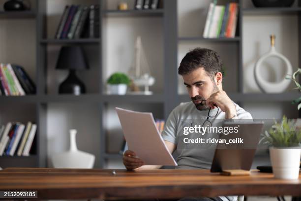a tired young adult manager reading candidate applications with a hand on his forehead. - document retention stock pictures, royalty-free photos & images
