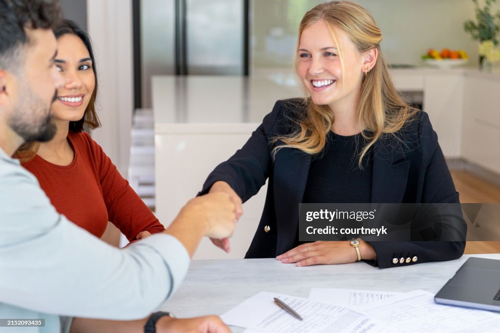 Real Estate or Insurance agent or lawyer shaking hands with couple. They are signing home loan mortgage or contract documents.