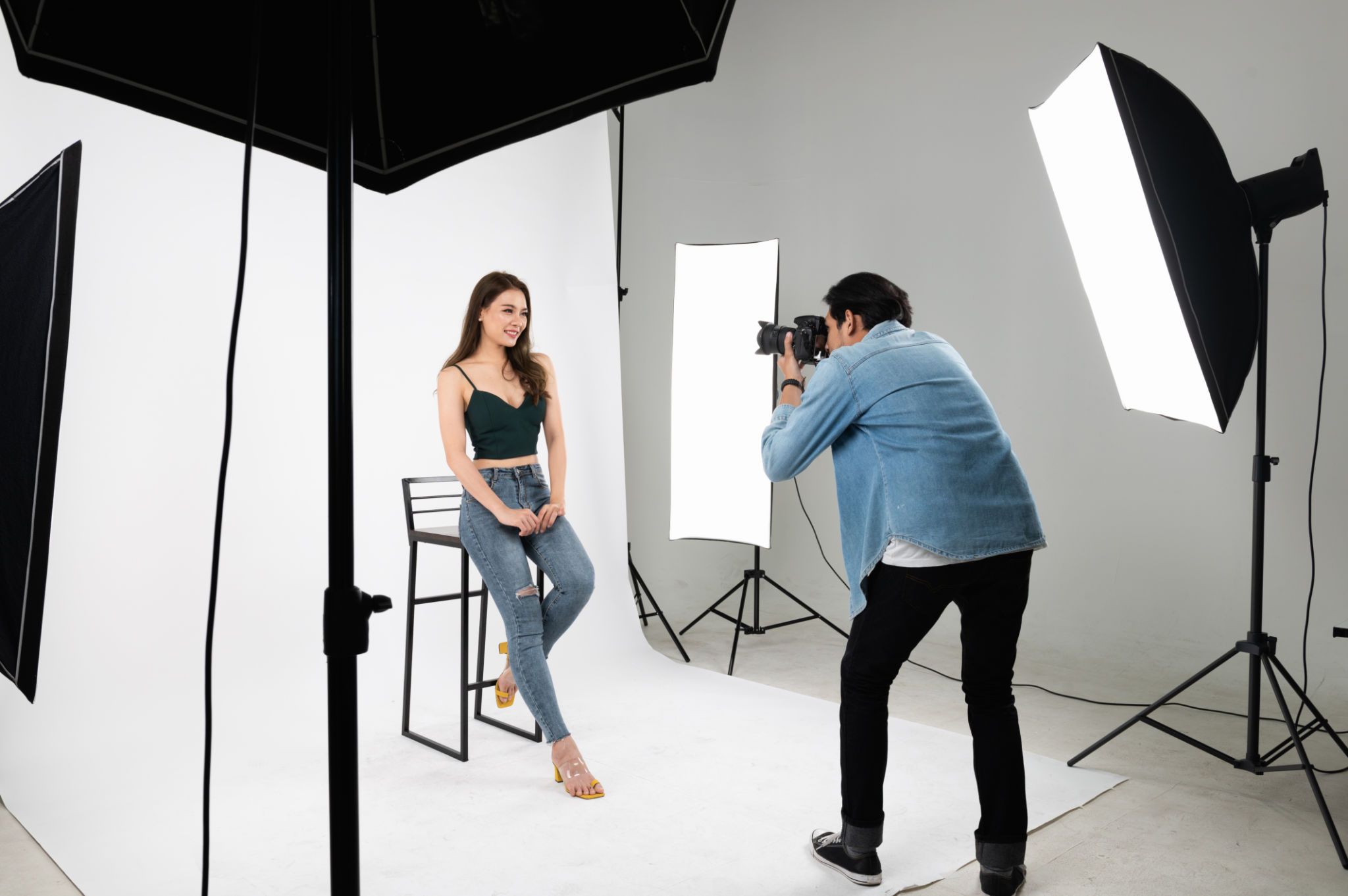 Professional male photographer taking photo of Asian woman in indoor studio with professional set of photographic equipment. Professional male photographer taking photo of Asian woman in indoor studio with professional set of photographic equipment.