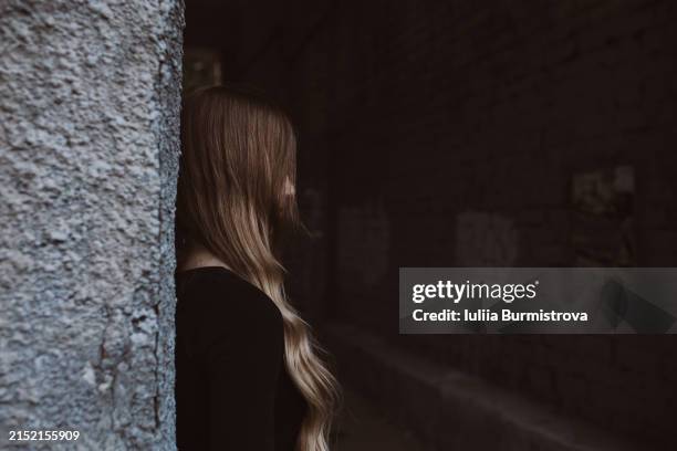 unrecognisable teen girl leaning against stone building, looking straight ahead, suggesting sense of quiet enjoyment of own company. - alleen één tienermeisje stockfoto's en -beelden