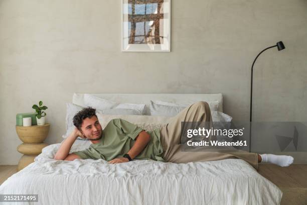 young man relaxing on bed in bedroom at home - bed pose stock pictures, royalty-free photos & images