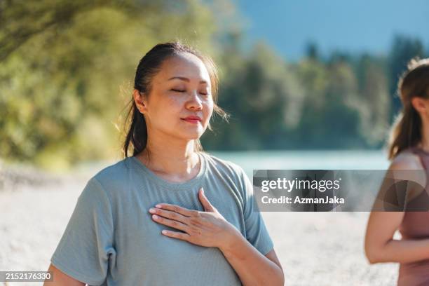 woman practicing yoga breathing exercise by the river - silence stock pictures, royalty-free photos & images