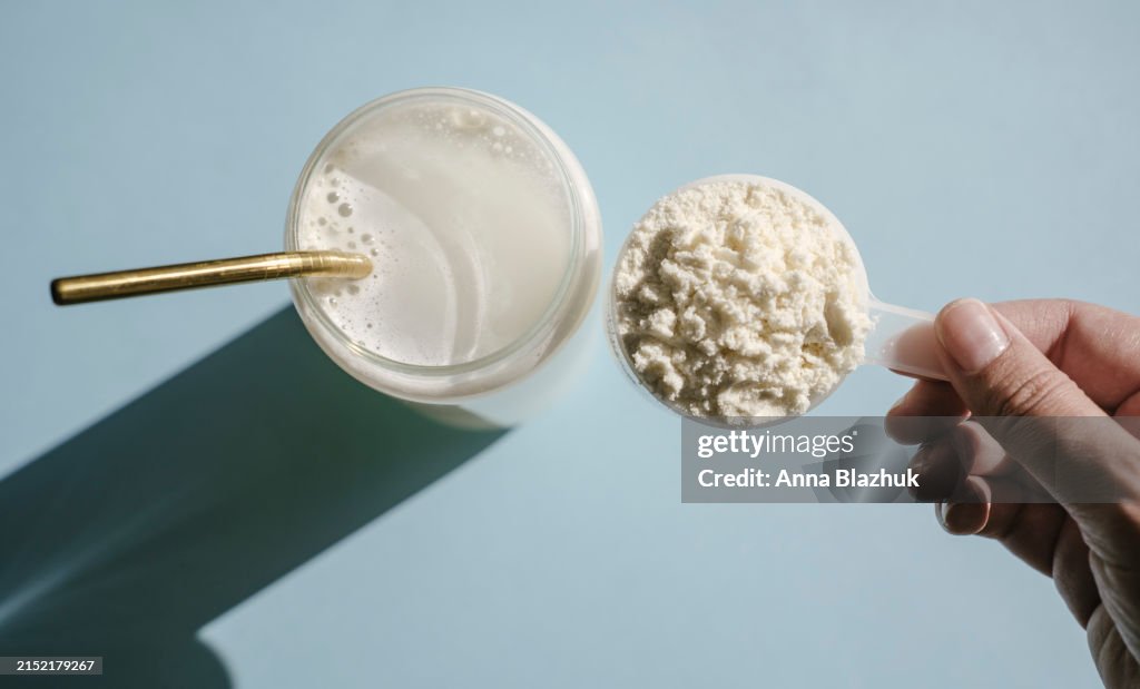 Protein isolate powder. Unflavored whey protein in measuring scoop and drinking glass in bright sunlight