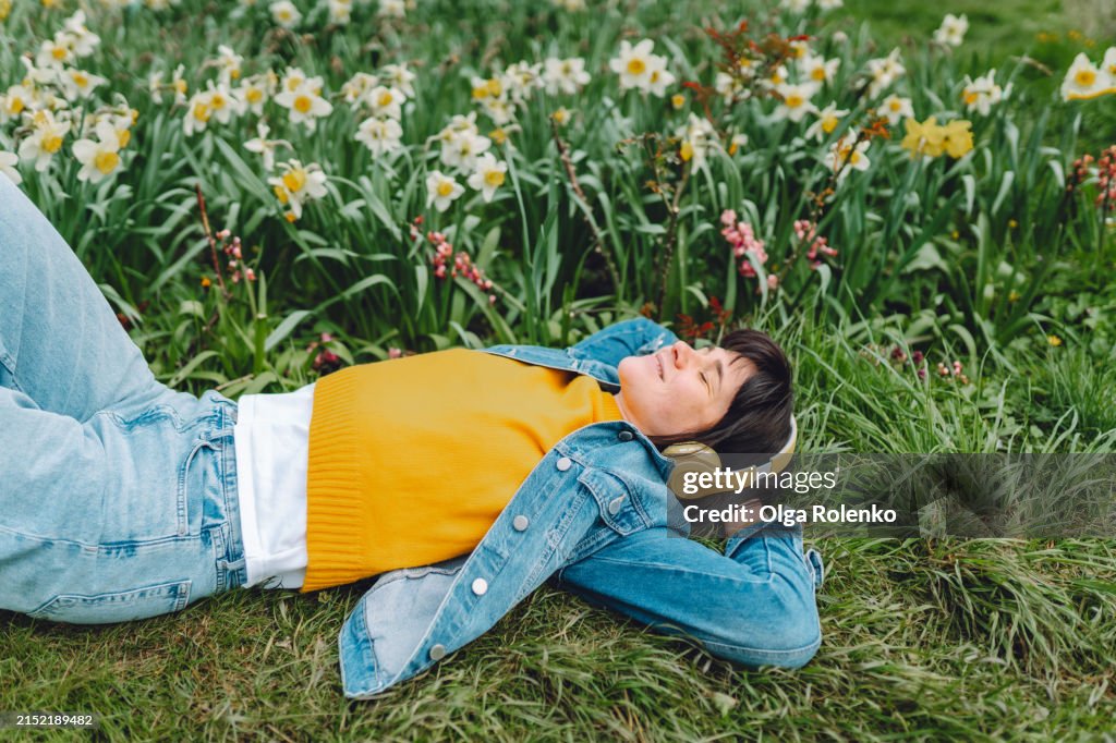 Serenity with headphones in the grass: young woman with headphones finds peace while lying in the grass of a spring park.