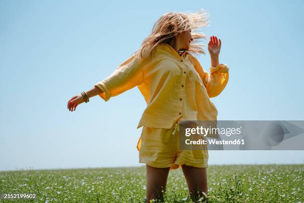 woman wearing yellow linen clothing with tousled hair in blooming field on sunny day - linen stock pictures, royalty-free photos & images