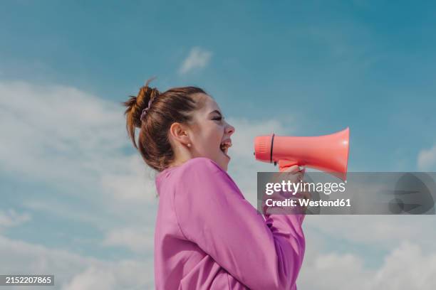 young woman screaming through megaphone under sky - megafono fotografías e imágenes de stock