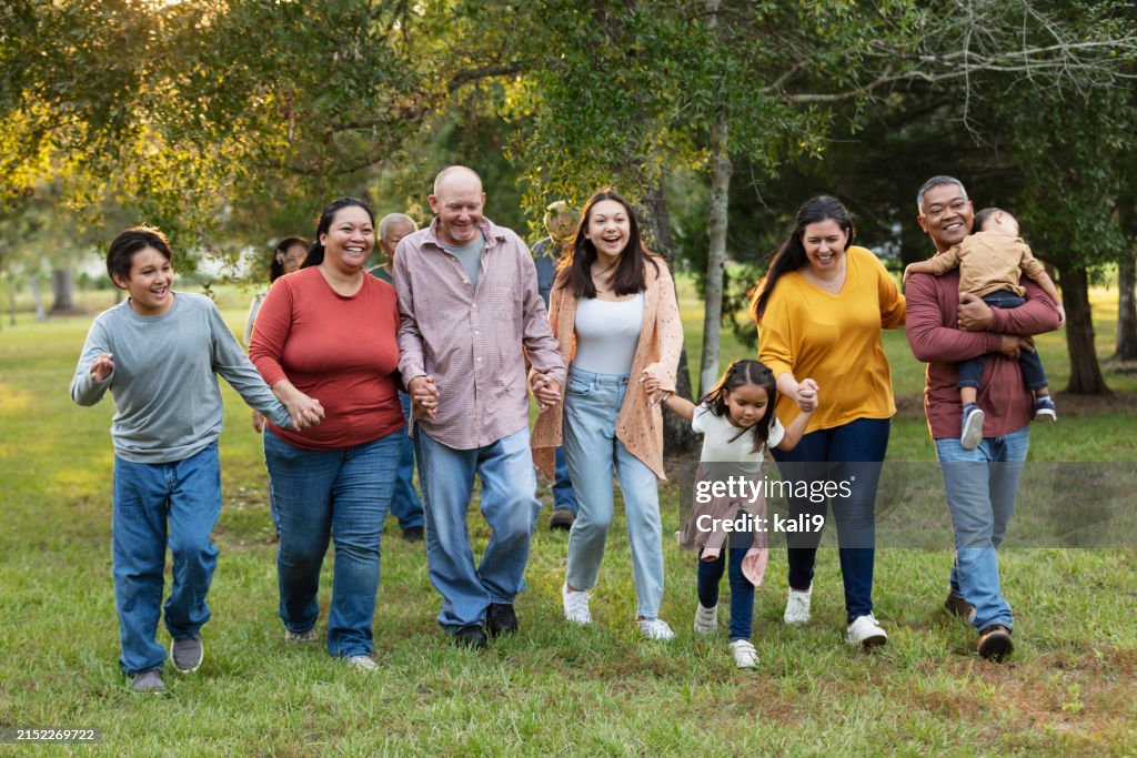 Multiracial extended family run playfully holding hands
