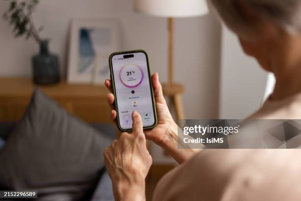 seniorin stellt thermostat in der smartphone-app ein - intelligenz stock-fotos und bilder