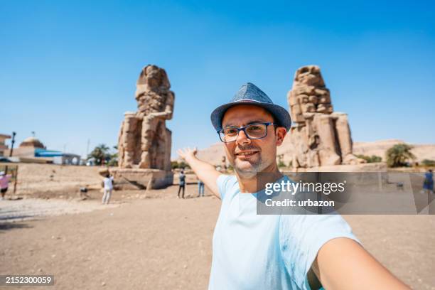 mid-adult man taking selfies at the colossi of memnon in luxor in egypt - colossi of memnon stock pictures, royalty-free photos & images