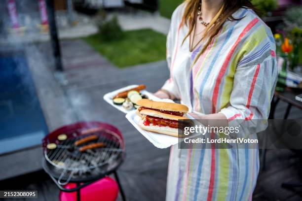 woman holding grilled food at a backyard barbecue party - processed meat stock pictures, royalty-free photos & images