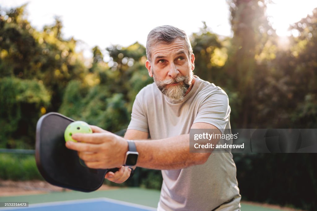 Elderly man serving at pickleball