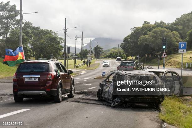 Motorist with the Socialist Kanak National Liberation Front flag drives past burnt cars in Noumea on May 14 amid protests linked to a debate on a...