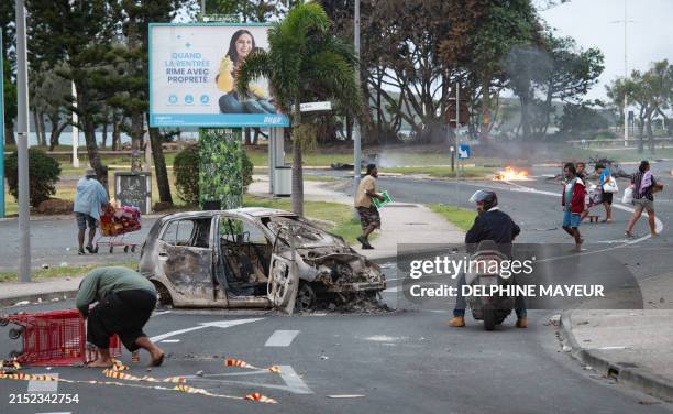 People walk down the street pushing shopping trolleys next to a burnt-out car after a supermarket was looted and shops vandalised in the N'Gea...